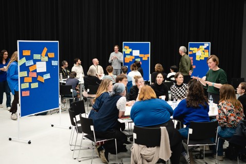 Viele Menschen sitzen an Tischen bei einem Workshop und erarbeiten auf Pinnwänden Ideen