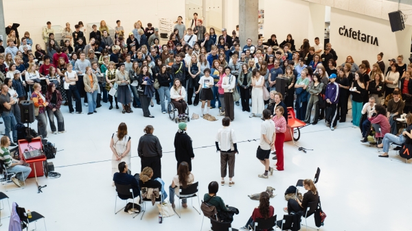 Foto der Begrüßung der neuen Studierenden: Fünf Redner*innen stehen im Atrium vor einer
                                          großen Gruppe Studierender.