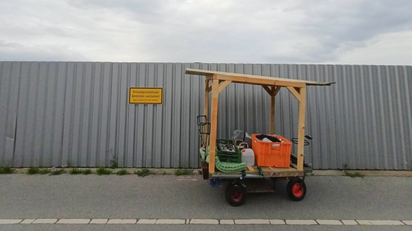 Ein Holzwagen vor einem metallenen
                                          Baustellenzaun