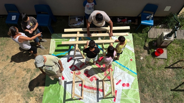 Kinder und Erwachsene arbeiten an einem Holzobjekt
                                          im Freien, , Summer School im Rahmen des Projekts Lunik CoLab