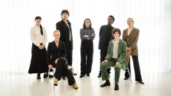Eine
                                          Gruppe von 7 Personen steht vor einem hellen weißen Hintergrund und posiert für die Kamera. 